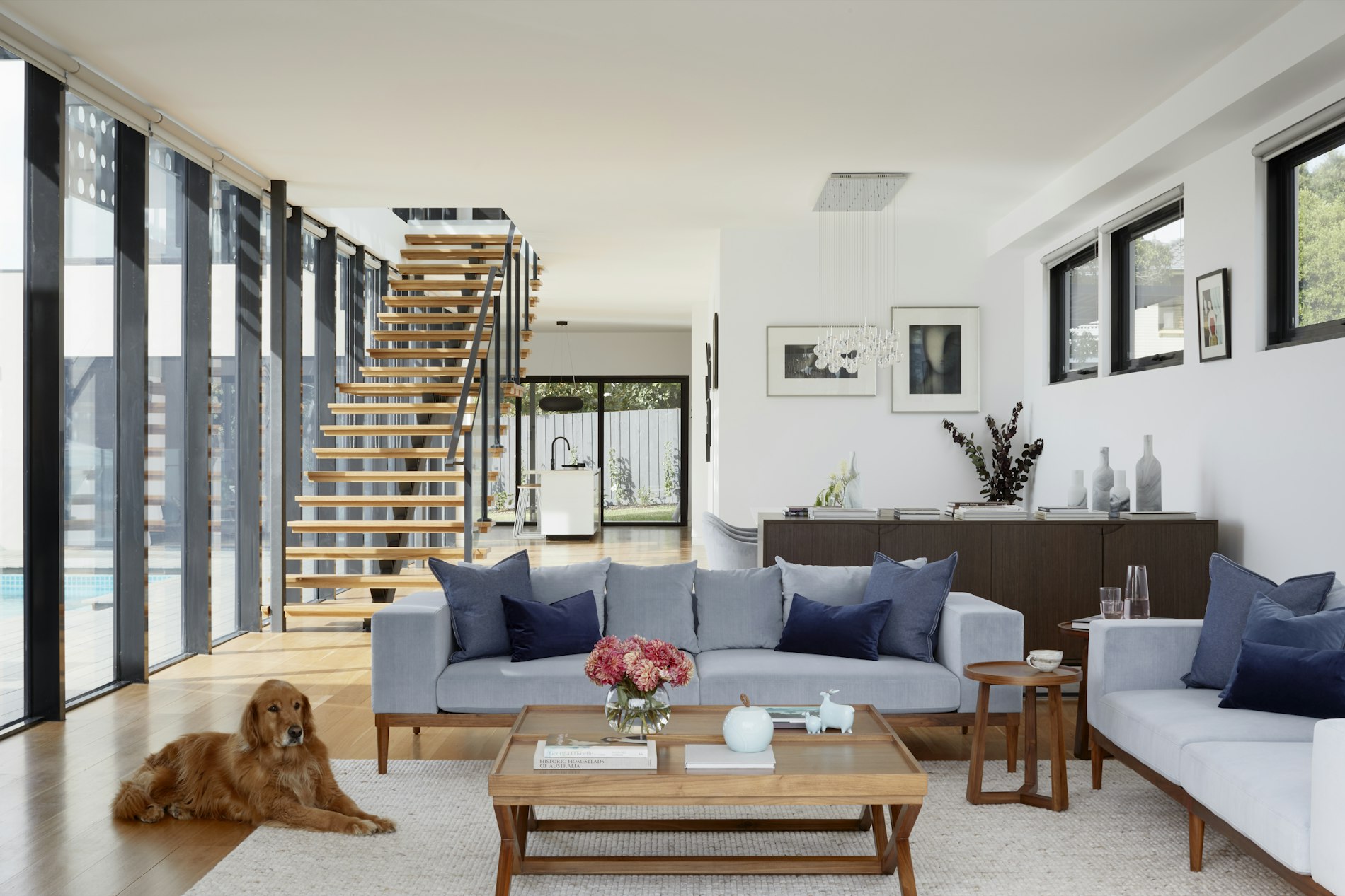 Bright open-plan living room with a floating staircase and pool view